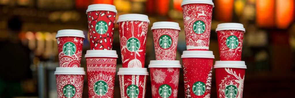 Twelve holiday Starbucks cups stacked in stacks of two with different sizes of red cups with white lids