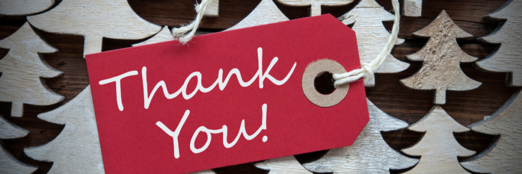 Red holiday thank you tag laying on small white wooden Christmas trees