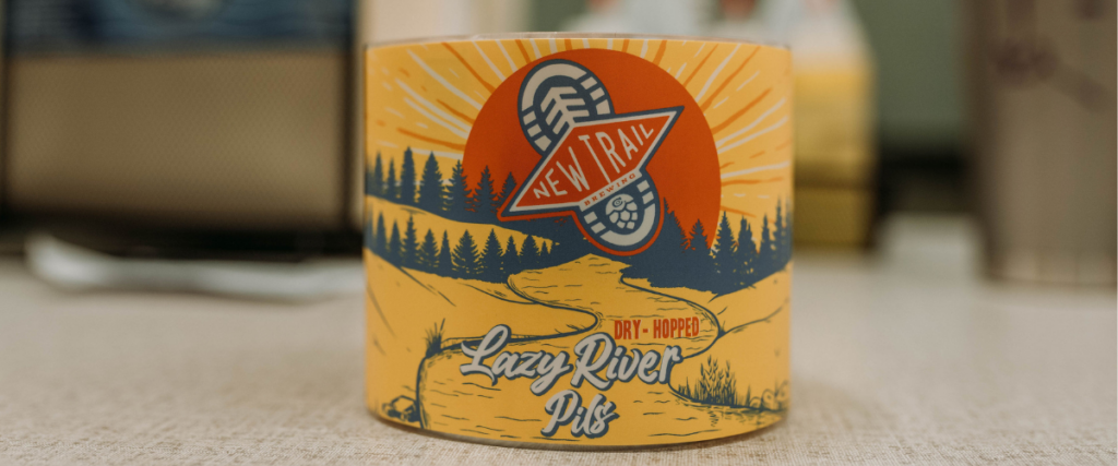 New Trail Brewing Lazy River Pils dry-hopped pilsner can label with sunset, forest, and river illustration